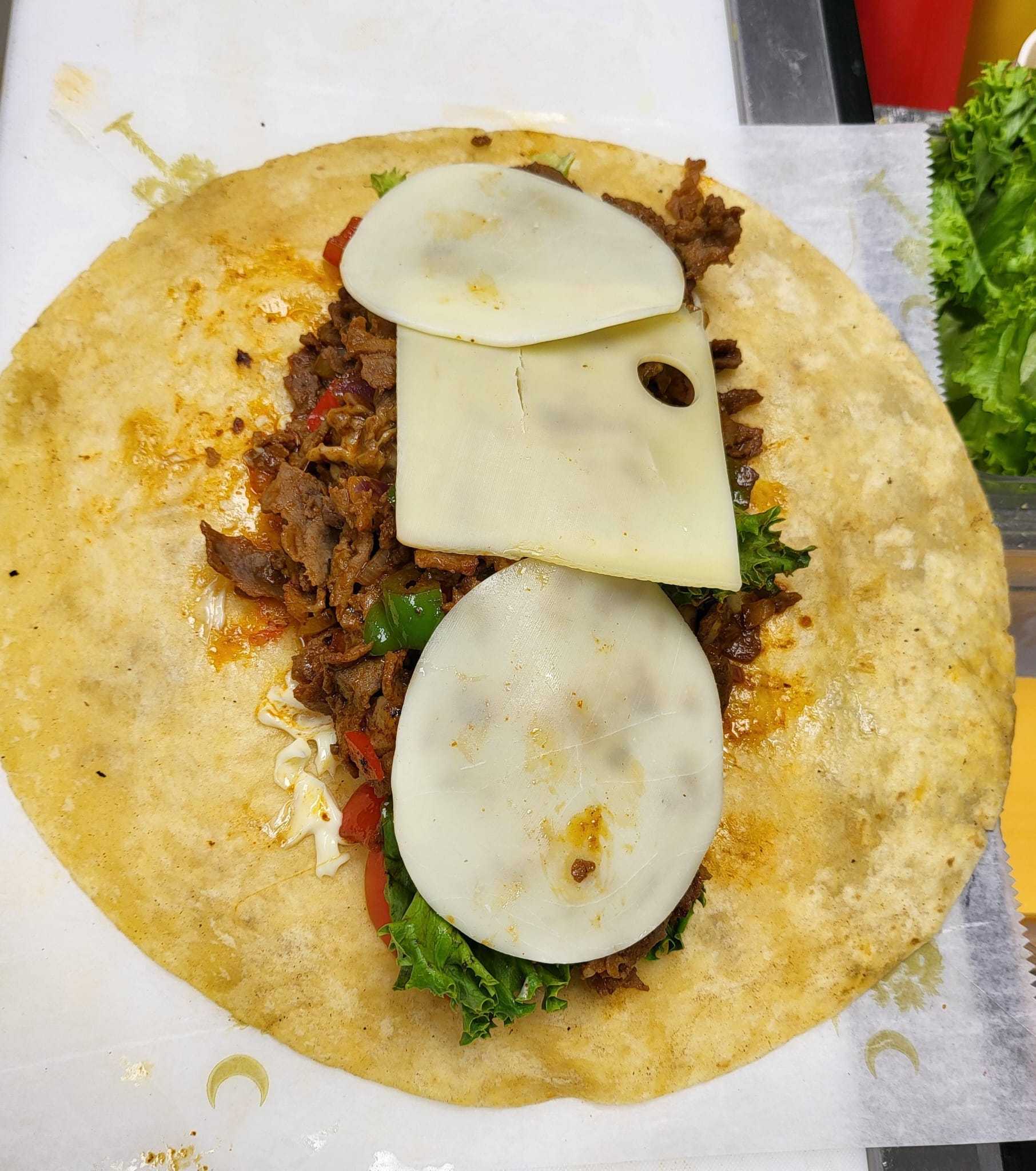 Open burrito with seasoned meat, vegetables, and two slices of cheese on a tortilla.