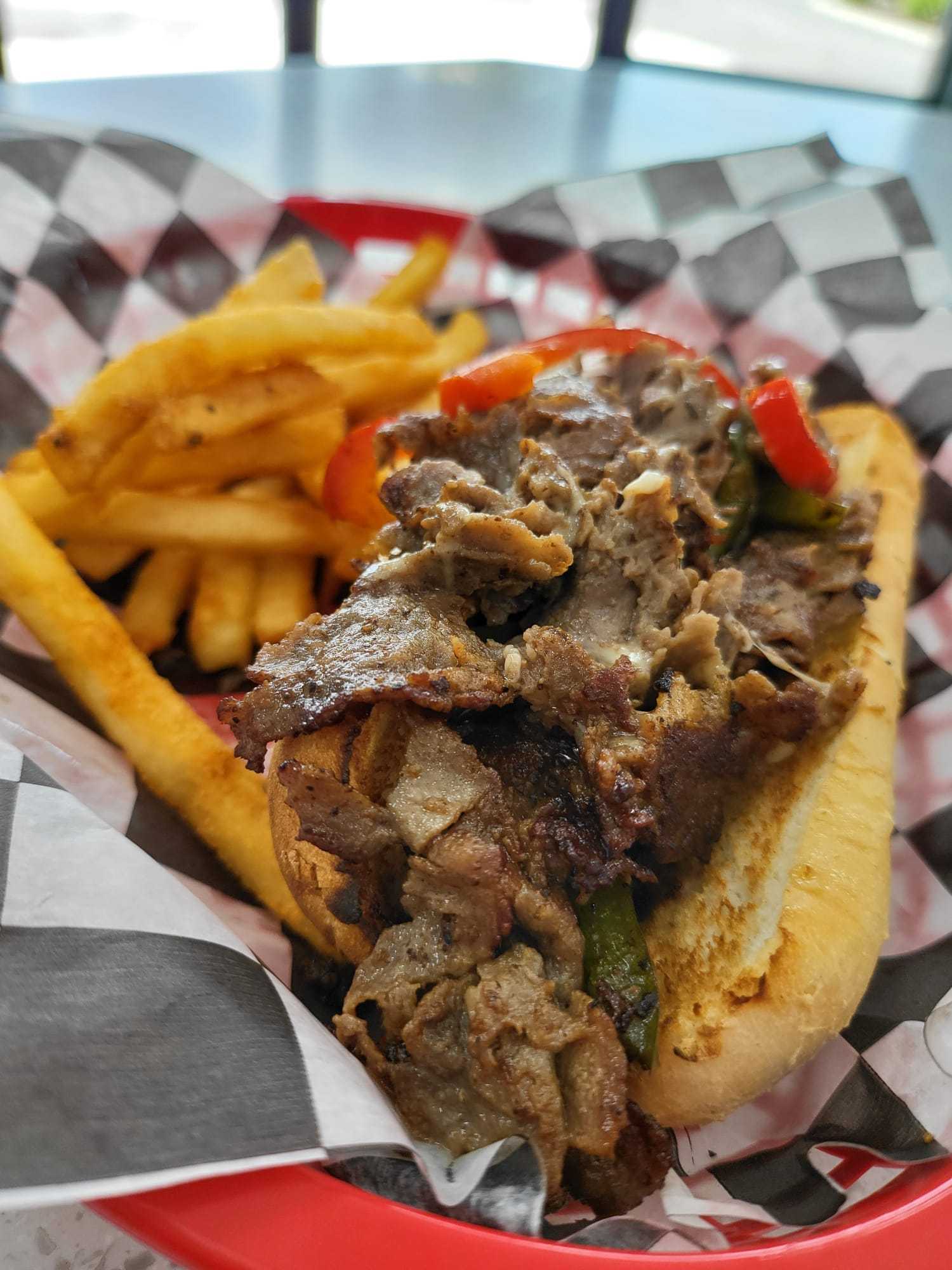 Philly cheesesteak with fries in a red basket on a checkered paper lining.