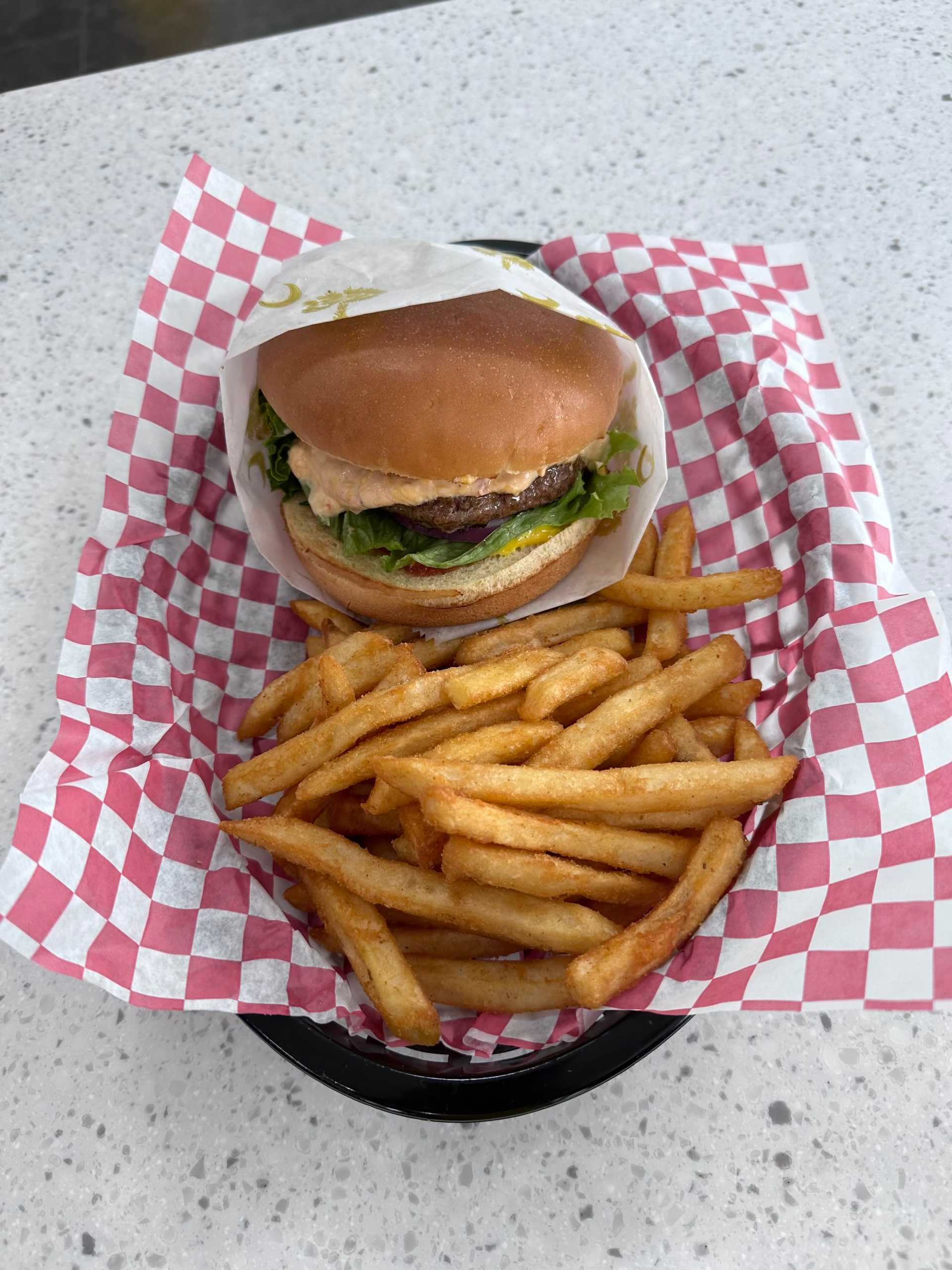 Burger with lettuce and sauce, served with crispy fries on red and white checkered paper.